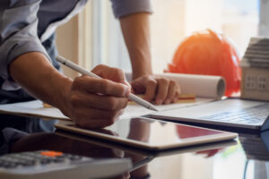 Architect man or male engineer work on digital tablet with blue print and laptop computer on the desk at office.